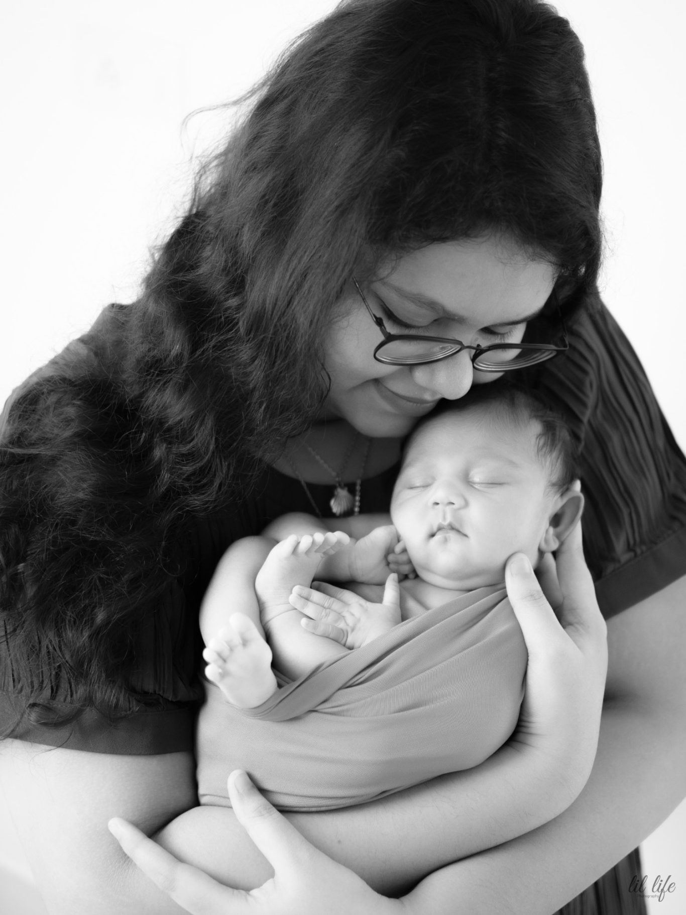 A woman holding a sleeping baby in her arms, both smiling gently.